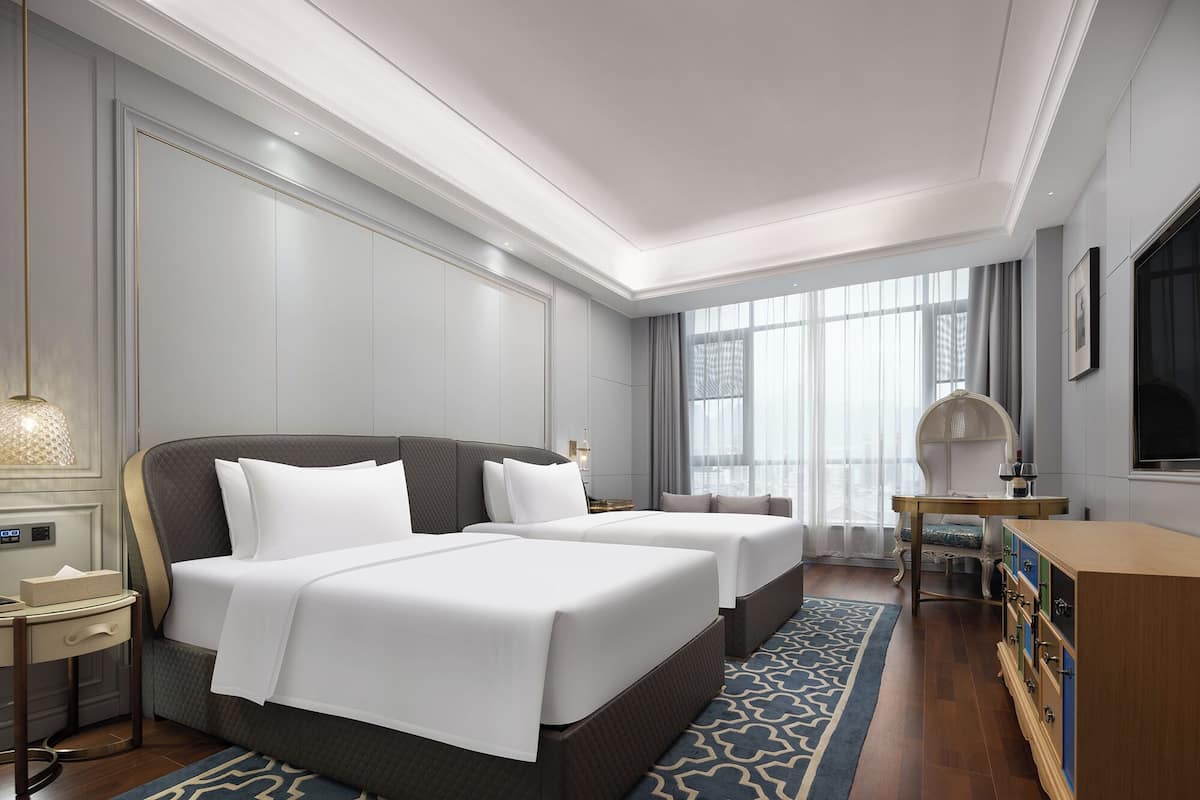Ein Hotelzimmer mit zwei Betten, einem Schreibtisch, einem Stuhl und einem großen Fenster.
