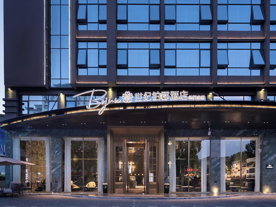 Entrada de hotel con diseño moderno, amplios ventanales de vidrio y un letrero iluminado llamativo.