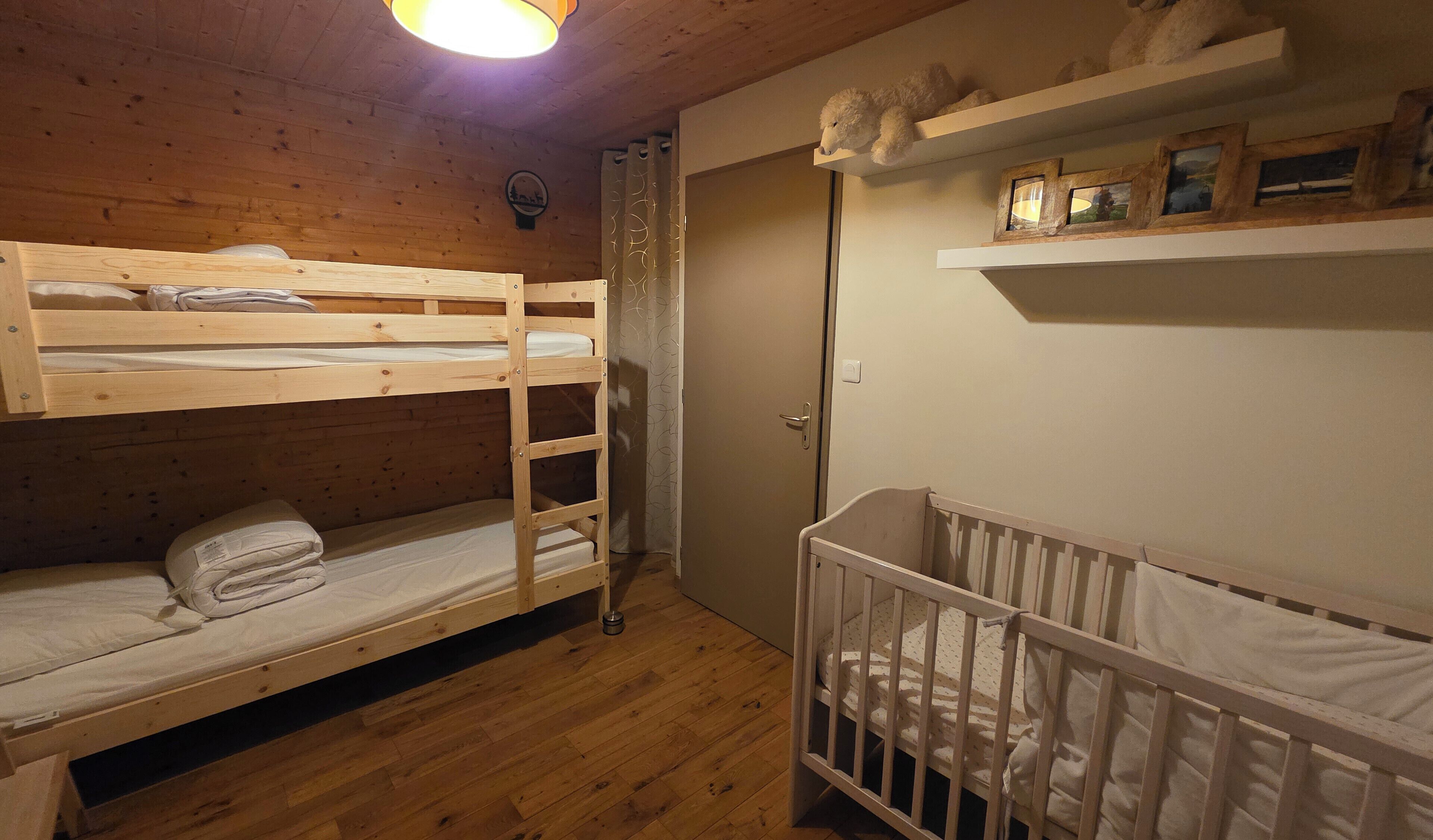 Een slaapkamer met stapelbed, ledikant, houten vloer en een deur waar een handdoek aan hangt.