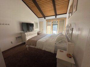 Ein Schlafzimmer mit Bett, Fernseher, Kommode, Spiegel und einem Fenster mit Aussicht.