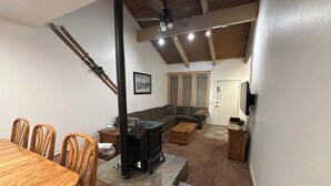 A living room with a fireplace, a sofa, a dining table with chairs, and a ceiling fan. - Bike, Hike & Unwind. Heated Pool, Hot Tub and Sauna. (Mammoth Lakes)