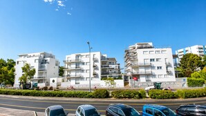 Un edificio residencial de varios pisos con balcones, estacionamiento y un cielo azul despejado.