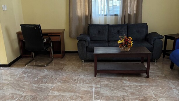 A living room with a sofa, a coffee table with a flower arrangement, a chair, and a window with curtains.