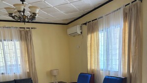 A room with a sofa, two blue armchairs, a small table, a lamp, and a ceiling fan.