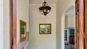 A hallway with a wooden door, a hanging light fixture, a framed picture, and a wicker basket with flowers. - Villa Adua | Blueapulia (Torre Suda)
