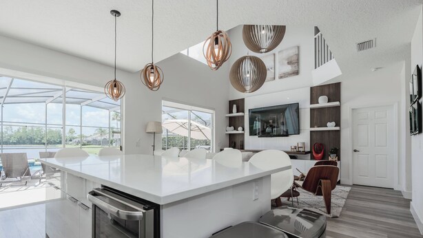 A modern kitchen with a large island, pendant lights, and a view of a pool. - Family Resort Pool Home Near Disney (Kissimmee)