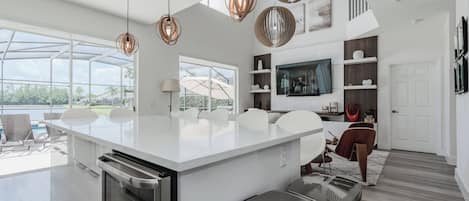 A modern kitchen with a large island, pendant lights, and a view of a pool.