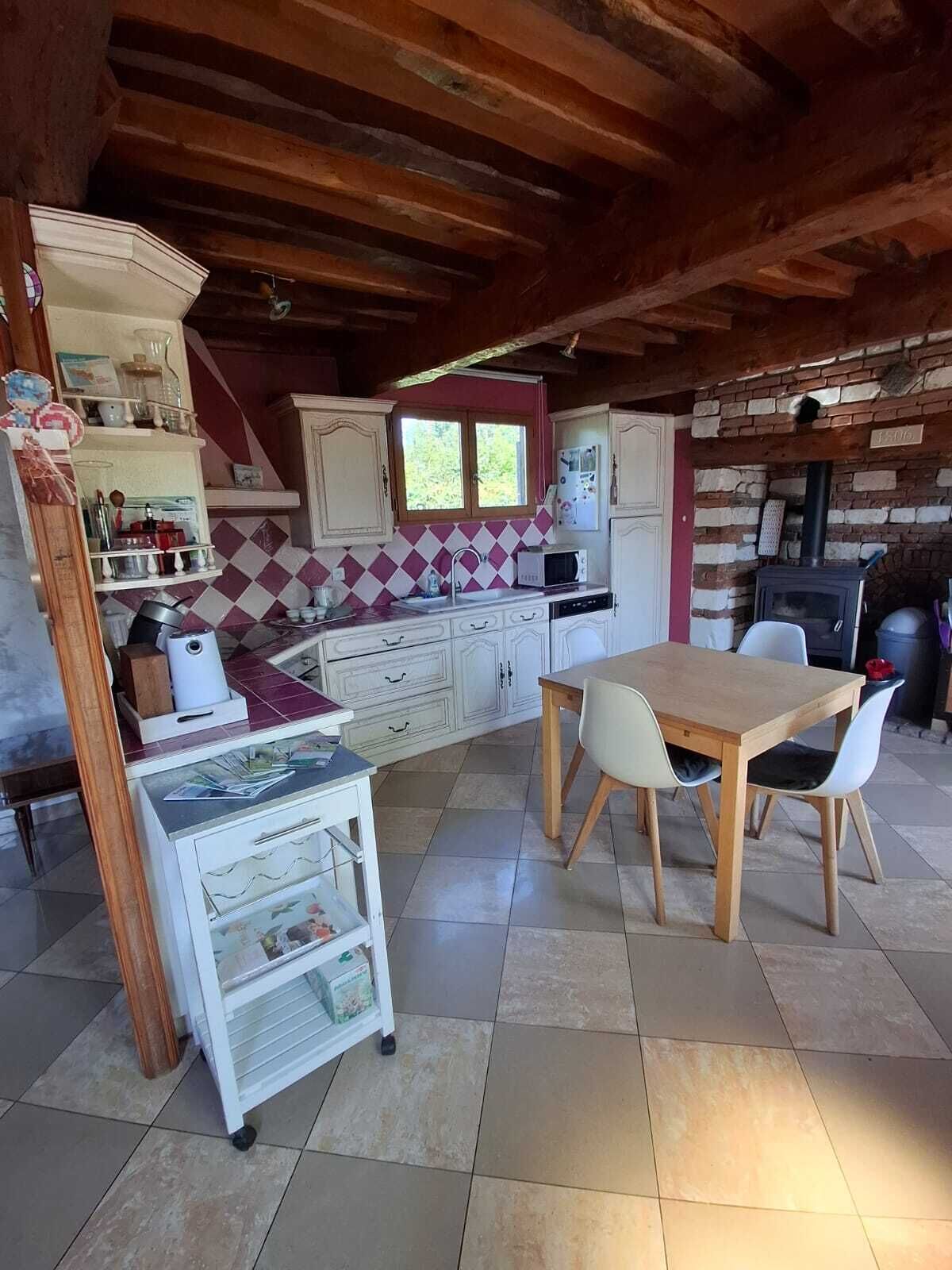 Una cocina rústica con techo de madera, piso de baldosas, una mesa de comedor con sillas y una estufa empotrada.