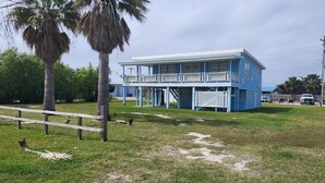 A blue building with a balcony, surrounded by grass and palm trees. - Waterview House by the Public Boat Ramp (Port O`Connor)