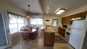 A kitchen with wooden cabinets, a white refrigerator, and a dining area with a table and chairs. - Waterview House by the Public Boat Ramp (Port O`Connor)