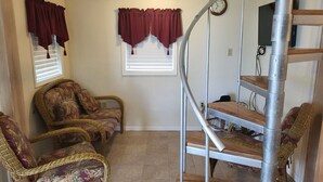 A room with a spiral staircase, two wicker chairs, a window with blinds, and a wall-mounted clock. - Waterview House by the Public Boat Ramp (Port O`Connor)