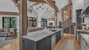 Une cuisine spacieuse dotée d’un grand îlot central, de poutres en bois et d’un coin repas offrant une vue sur l  ’extérieur.
