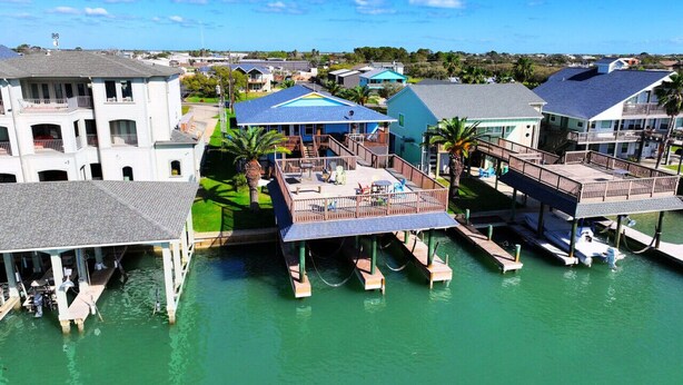 A waterfront property with multiple docked boats, a covered deck area, and residential buildings. - Beautiful Intracoastal Home with Two Boat Lifts and a Boat Slip (Port O`Connor)