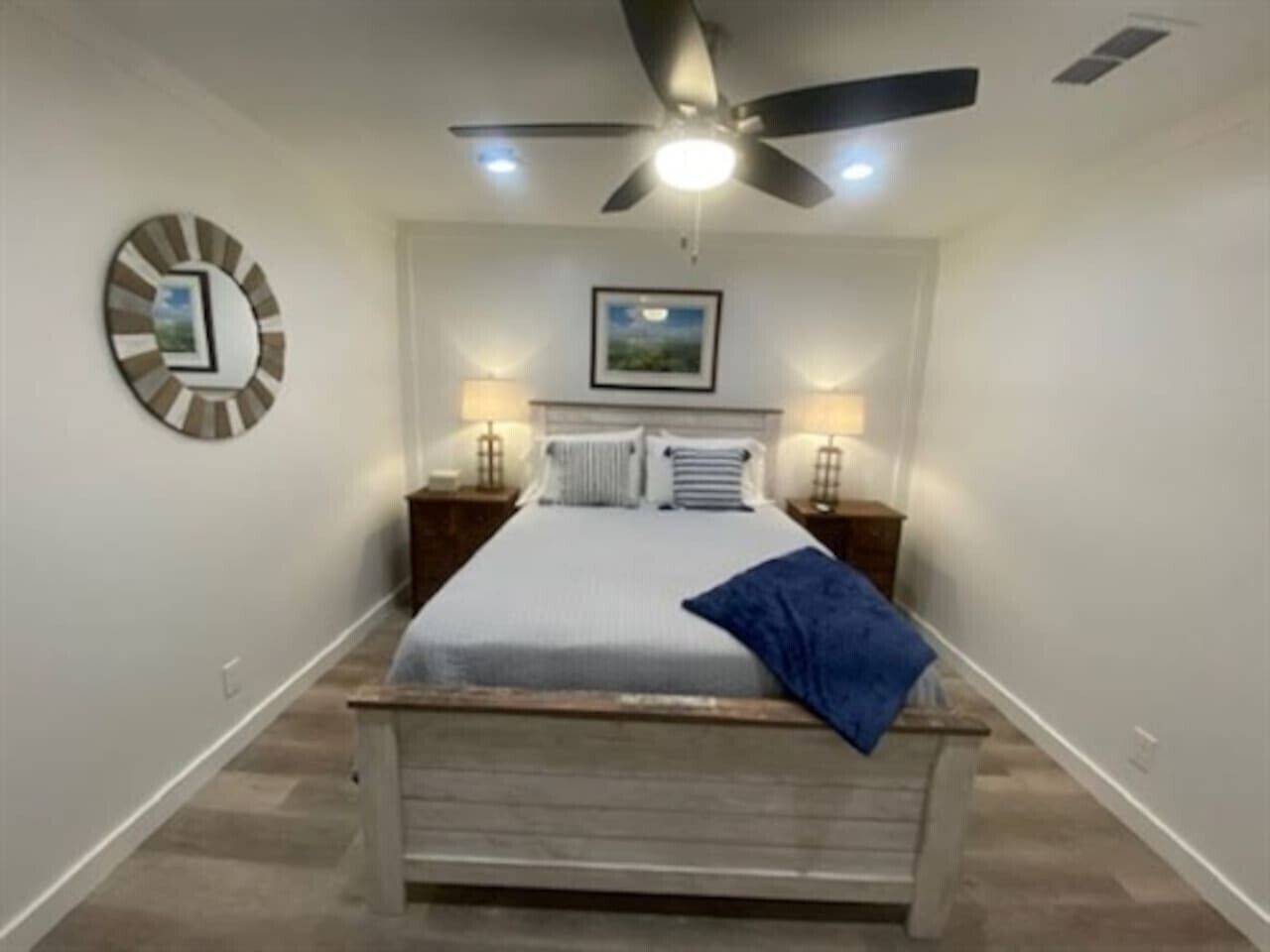 Um quarto com uma cama, um ventilador de teto, um relógio de parede e uma moldura com um quadro.