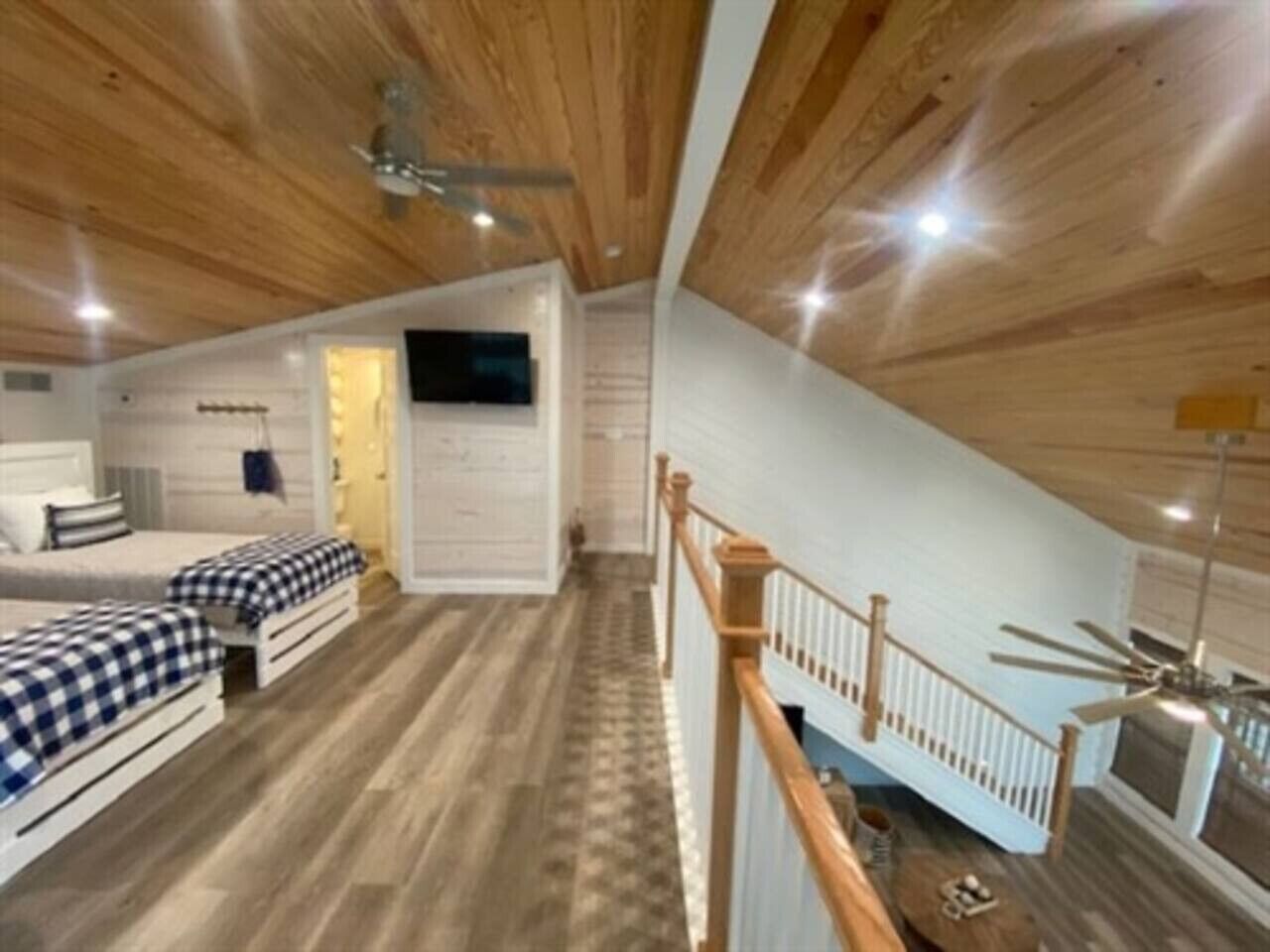Ett sovrum i loftstil med ett träpanelat tak, en säng med rutigt sänglinne, en liten sittgrupp och en trappa.