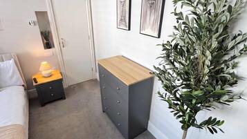 A modern bedroom with a bed, bedside table, lamp, dresser, and a potted plant.