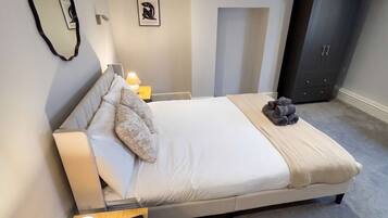 Een moderne slaapkamer met een groot bed, nachtlampjes, een klein tafeltje met lamp, een garderobe en een spiegel aan de muur.