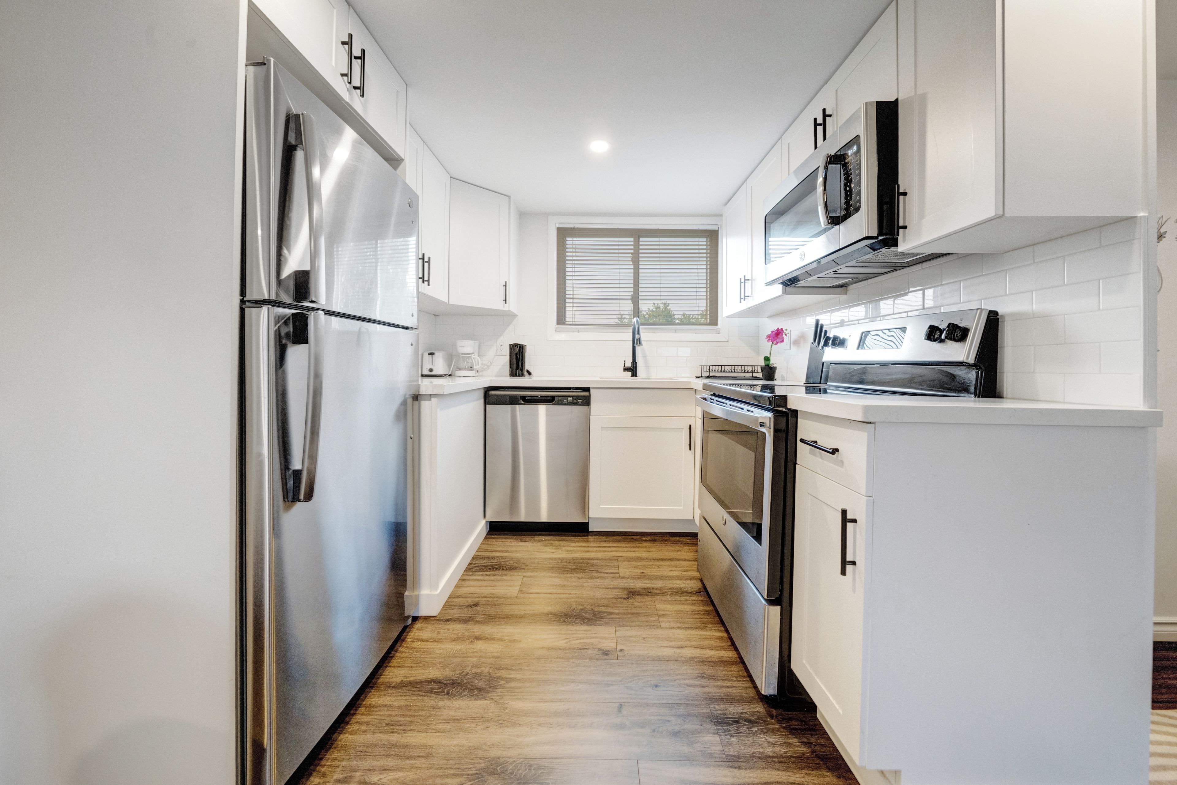 A modern kitchen with stainless steel appliances, white cabinetry, and a wooden floor.