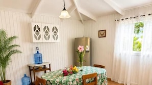 A dining area with a table set for two, wooden chairs, a hanging light fixture, and a window with curtains. - Cabañas Anariki - Rapa Nui  (Hanga Roa)
