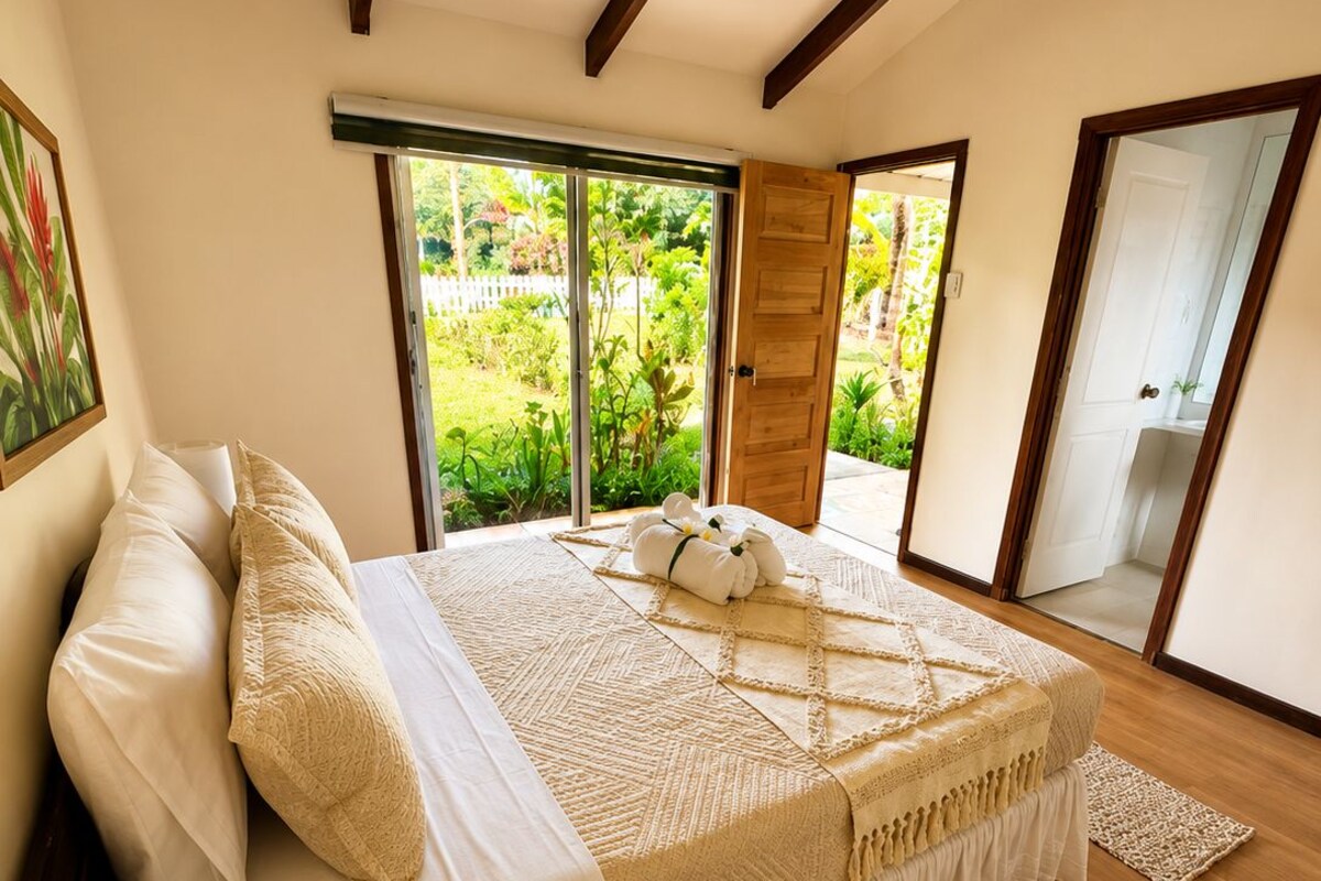 A bedroom with a bed, a bedside lamp, a plant, and a view of a garden through a sliding door.
