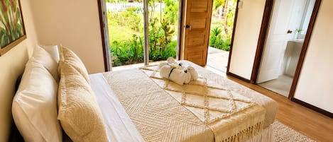 A bedroom with a bed, a bedside lamp, a plant, and a view of a garden through a sliding door.