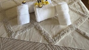 A neatly made bed with a quilt, two towels with decorative flowers, and bedside lamps on a white nightstand. - Cabañas Anariki - Rapa Nui  (Hanga Roa)