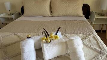 A neatly made bed with a quilt, two towels with decorative flowers, and bedside lamps on a white nightstand.