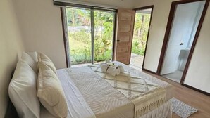 A bedroom with a large bed, a window, and a door leading to an outdoor area. - Cabañas Anariki - Rapa Nui  (Hanga Roa)