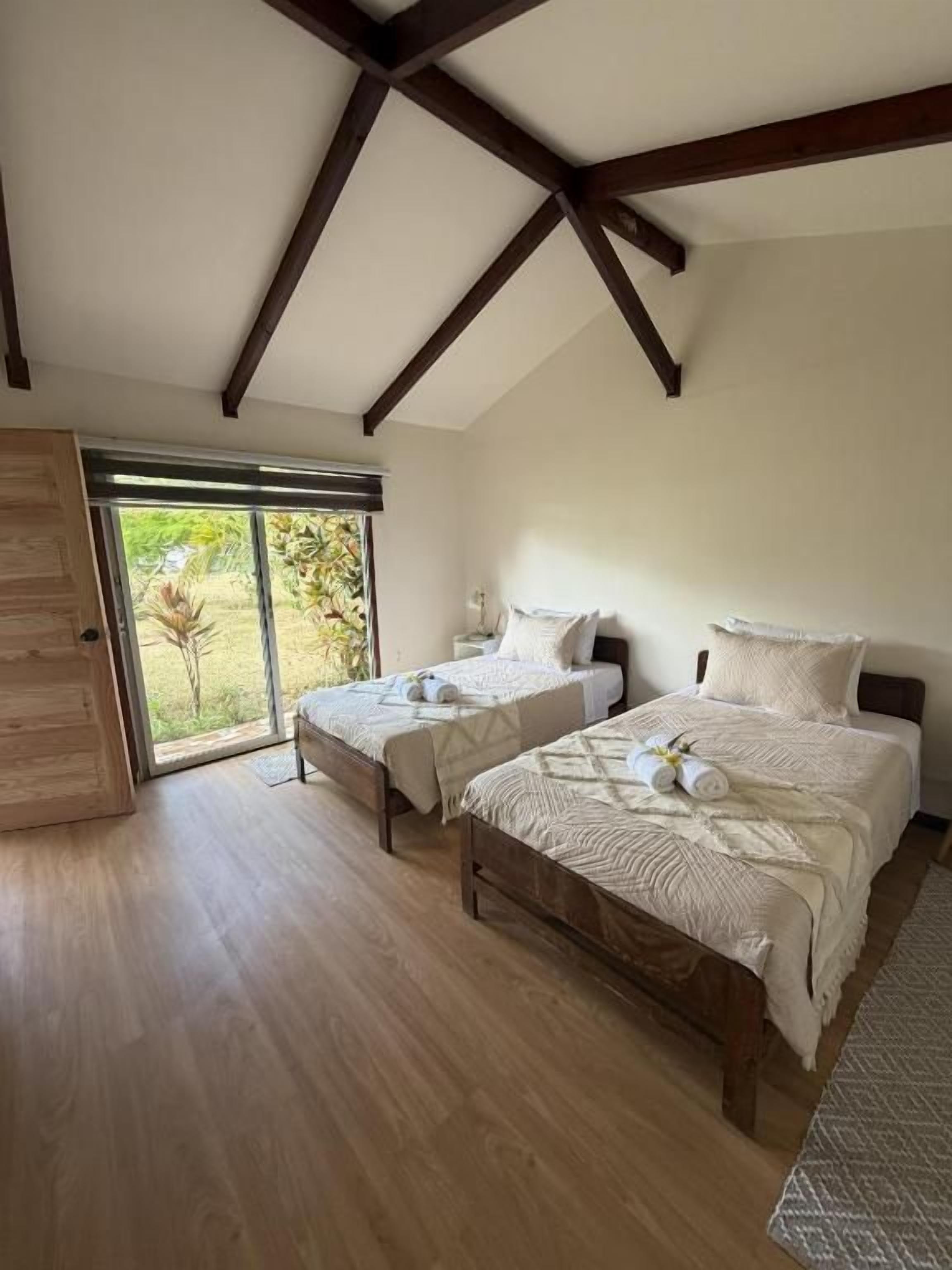 Un dormitorio con dos camas, suelo de madera, un ventanal grande y techo inclinado.