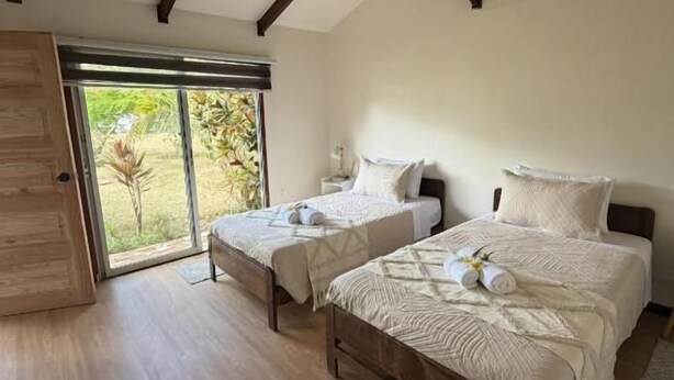 A bedroom with two beds, wooden flooring, a large window, and a sloped ceiling. - Cabañas Anariki - Rapa Nui  (Hanga Roa)