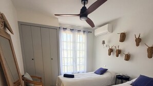 A room with two beds, a ceiling fan, a window with curtains, a wooden floor, and wall-mounted animal horns. - Villa Cap d'Antibes, a 2-minute walk from the beaches. (Antibes)