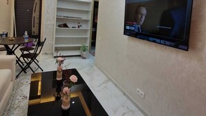 A modern living room with a flat-screen TV mounted on the wall, a black coffee table with vases, a sofa, and a dining area with chairs. - 
Apartment cosy modern and luxury Marrakech (Marrakesh)