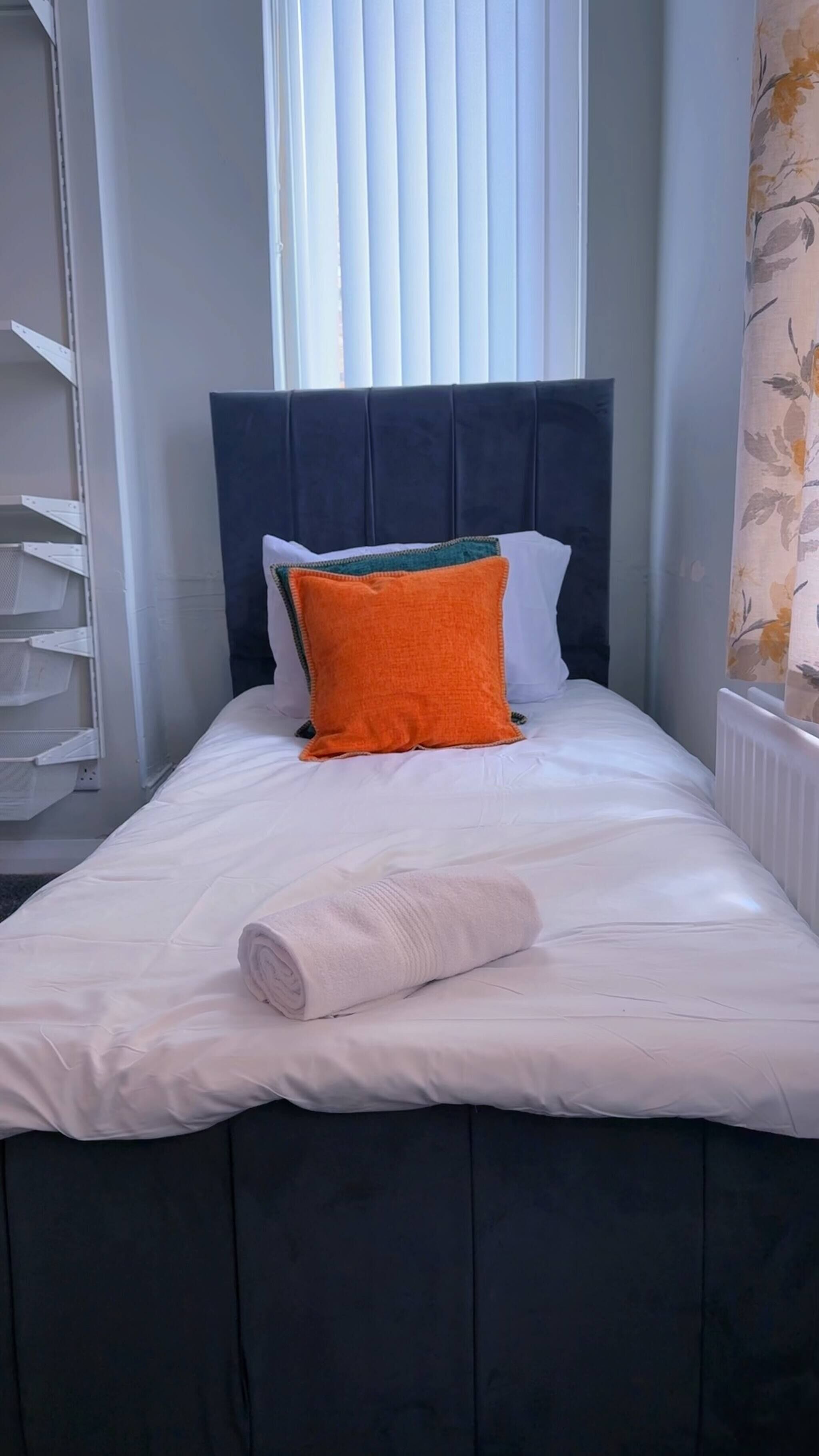 Una cama con cabecera oscura, ropa de cama blanca y una toalla blanca enrollada.