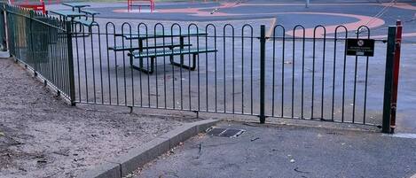 A playground with swings and climbing structures, surrounded by a metal fence.