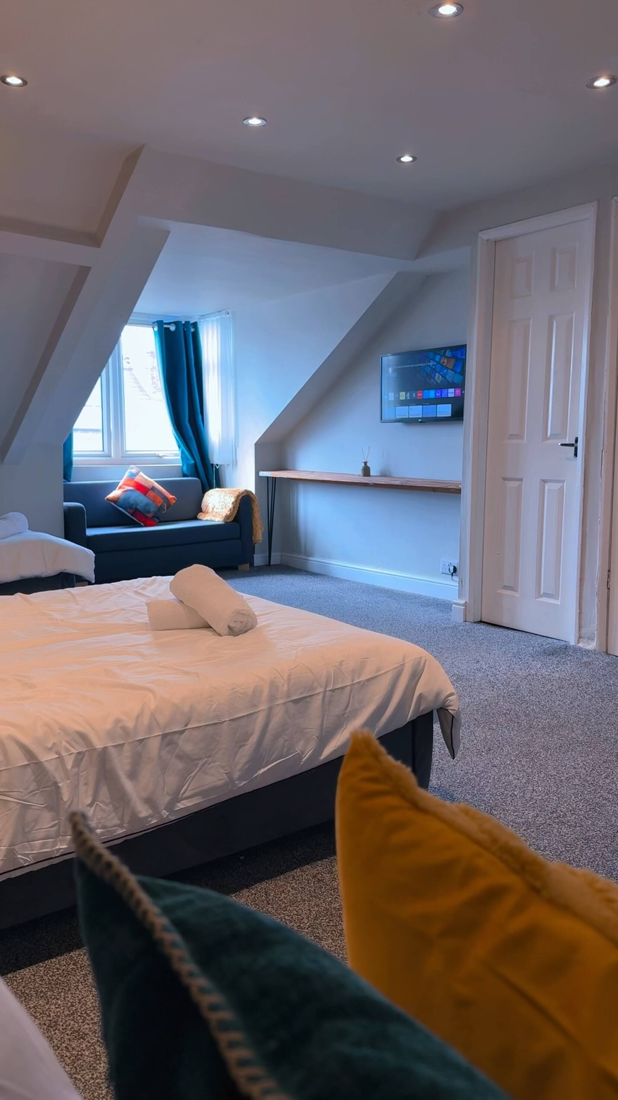 Une chambre avec un lit, une fenêtre avec des rideaux, un téléviseur fixé au mur et une porte.