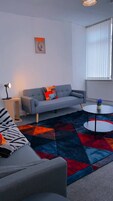 Una sala de estar moderna con un sofá gris, un tapete estampado, una mesita redonda y una ventana con persianas.