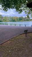 Un sendero pavimentado junto a un lago, con un cartel que indica una zona de esparcimiento para perros.