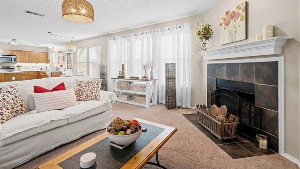 Een woonkamer met een open haard, een witte bank, een salontafel en een keuken op de achtergrond.