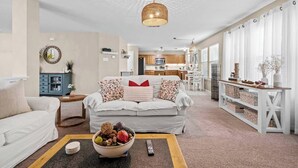 Een woonkamer met een bank, een salontafel met fruit, een televisie en een keuken op de achtergrond.