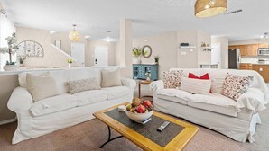 Een moderne woonkamer met twee witte banken, een salontafel en een keuken op de achtergrond.