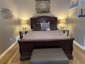 Ein Schlafzimmer mit einem großen Bett, zwei Nachttischlampen, einem hölzernen Kopfteil und einem dekorativen Wandbild.
