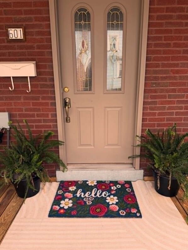 A front door with a number plate, a doormat with 'hello' and floral patterns, and two potted plants on either side. - The Heart of Huntingdon. Gorgeous 4-bedroom house with character, in Huntingdon. (Huntingdon)