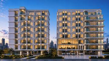 A modern multi-story hotel with balconies, large windows, and a parking area.