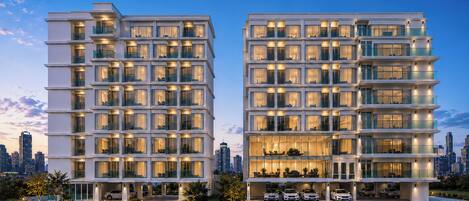 Un hotel moderno de varios pisos con balcones, ventanas amplias y una zona de estacionamiento.