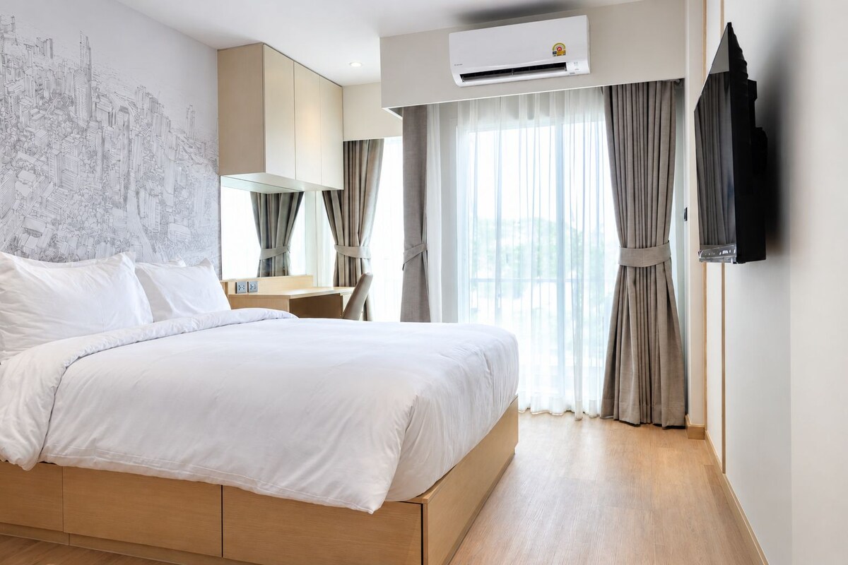 Habitación de hotel con una cama grande, un escritorio, un equipo de aire acondicionado y un mural de un paisaje urbano en la pared.