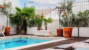 Zona de piscina en la azotea con terraza de madera, sillas reclinables y plantas en macetas.