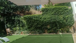 Un patio con césped artificial, una silla de madera y una pared cubierta de hiedra.
