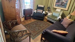 A living room with a ceiling fan, a patterned rug, a wooden cabinet, and a sofa with cushions. - 2-bedroom apartment 0.1miles from Forsyth Park, steps from Kroger and parking.  (Savannah)