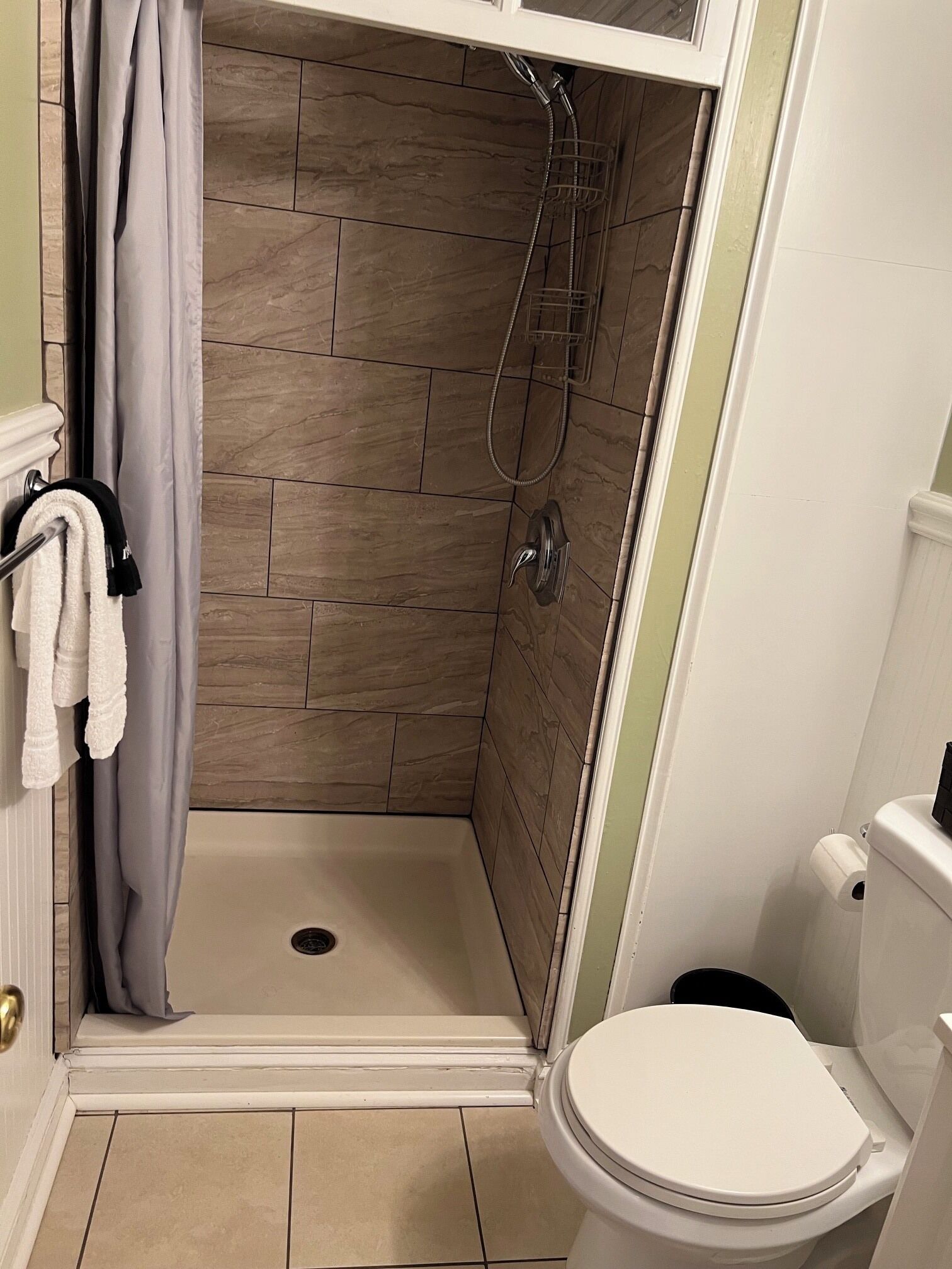 A bathroom with a shower, toilet, and a towel rack with towels.
