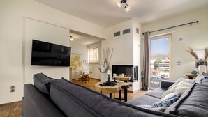 Ein modernes Wohnzimmer mit einem großen grauen Sofa, einem Flachbildfernseher, einem Kamin und einem Balkon mit Blick.